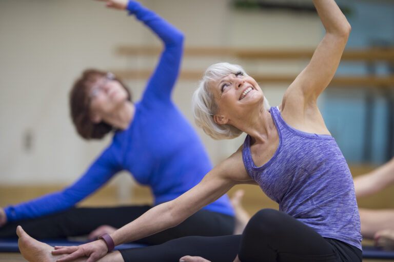 A multi-ethnic group of senior adult women are taking a yoga class together at the gym.